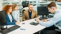 Ein Automobilkaufmann berät eine junge Familie beim Autokauf im Autohaus.