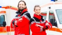 Ein Rettungssanitäterteam in roter Uniform steht vor zwei Krankenwägen, bereit für den nächsten Einsatz.