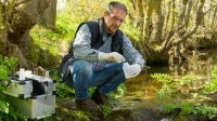 Eine Fachkraft für Wasserwirtschaft entnimmt Proben zur Überprüfung der Wasserqualität eines Flusses.