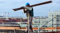 Ein Gerüstbauer transportiert Holzbretter für ein Gerüst auf einer Baustelle.
