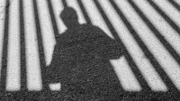 Man sieht den Schatten einer Person hinter dem Schatten von Gitterstäben.