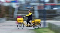 Eine Fachkraft für Kurier-, Express- und Postdienstleistungen der Deutschen Post fährt mit ihrem Dienstfahrrad durch ein Wohngebiet in Schwerin.
