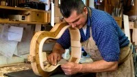 Ein Zupfinstrumentenmacher schleift die Seitenwand eines Gitarrenkorpus.