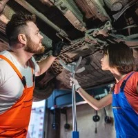 Eine Kraftfahrzeugmechatronikerin und ein Kraftfahrzeugmechatroniker überprüfen ein Auto in der Werkstatt.