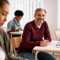 Ein Mann sitzt mit anderen in einem Klassenzimmer