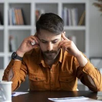 Ein Berufsschullehrer sitzt zuhause am Schreibtisch und stützt den Kopf auf die Hände.