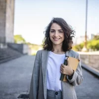 Junge Frau mit Buch steht vor einem Gebäude mit Säule