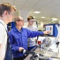 Ein Ausbilder zeigt zwei Auszubildenden die Bedienung einer Maschine