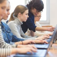 Mehrere Schülerinnen sitzen an Laptops, die Lehrerin erklärt etwas am Bildschirm einer Schülerin.