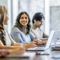 Fotografie von drei Frauen und einem Mann, die vor ihren Laptops sitzen und lernen.