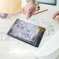 Auf einem Tisch liegt eine Bauzeichnung, auf der wiederum ein Tablet mit einem Hologramm eines Hauses sowie ein Lineal, Helm und Stift liegen. Eine Hand berührt das Hologramm.