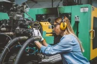 Eine Anlagemechanikerin überprüft eine CNC-Maschine, die Werkstücke mit hoher Präzision automatisch herstellt.