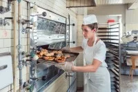 Eine Bäckerin holt frisch gebackene Brezeln und Brötchen aus dem Ofen.