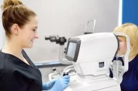 Eine Orthoptistin führt einen Sehtest mit einem medizinischen Gerät bei einem Kind durch.