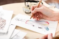 Eine Modedesignerin skizziert auf ihrem Schreibstift mit einem Buntstift und Papier verschiedene bunte Kleider. 