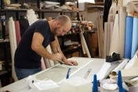 Ein Buchbinder bestreicht die Pappen für den Einband eines Buches mit Leim. 