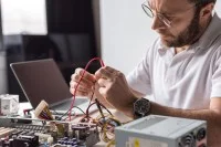 Ein Assistent für Wirtschaftsinformatik tüftelt an seinem Schreibtisch an der Hardware eines auseinandergebauten Computers.