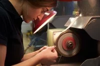 Eine Edelsteinschleiferin schleift einen sogenannten Lagestein in einen Goldring ein.