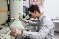 Ein physikalisch-technischer Assistent betrachtet eine Probe am Elektronenmikroskop und stellt dabei die Messwerte ein.