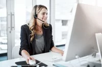 Eine kaufmännische Assistentin / Wirtschaftsassistentin für Informationsverarbeitung führt ein Telefongespräch mit einem Headset, während sie vor ihrem Computer im Büro sitzt.