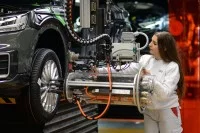 Eine Fertigungsmechanikerin bringt an einem Fließband ein Rad an einem Auto an. 