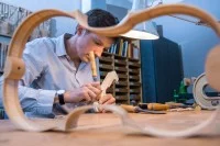 Ein Geigenbauer schnitzt in seiner Werkstatt am Schneckenkopf für den Nachbau einer historischen Geige.