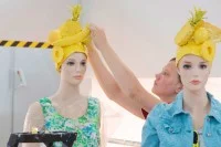 Eine Gestalterin für visuelles Marketing schmückt zwei Schaufensterpuppen mit augefallenen Kopfbedeckungen.