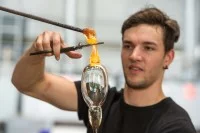 Ein Glasmacher formt aus erhitztem Glas ein Gefäß.