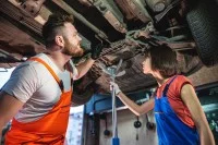 Eine Kraftfahrzeugmechatronikerin und ein Kraftfahrzeugmechatroniker überprüfen ein Auto in der Werkstatt.