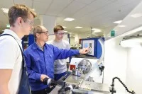 Ein Ausbilder zeigt zwei Auszubildenden die Bedienung einer Maschine