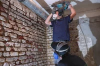 Zwei Holz- und Bautenschützer arbeiten an einer Ziegelwand.