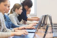 Mehrere Schülerinnen sitzen an Laptops, die Lehrerin erklärt etwas am Bildschirm einer Schülerin.