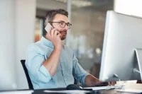 Ein kaufmännischer Assistent / Wirtschaftsassistent für E-Business Management sitzt an seinem Schreibtisch und telefoniert, während er auf seinen Computerbildschirm schaut.