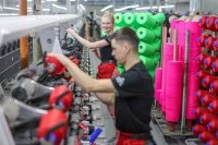 Zwei Mitarbeiter einer Spulerei für Textilveredlung wechseln Spulen mit farbigem Garn. 