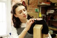 Eine Sattlerin näht in der Werkstatt an einer Tasche.