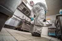 Ein Schädlingsbekämpfer versprüht in einer Küche Chemikalien zur Schabenbekämpfung.