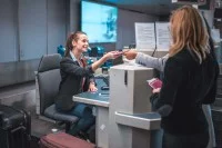 Eine Servicekauffrau im Luftverkehr prüft am Check-in-Schalter die Pässe von zwei Passagieren.