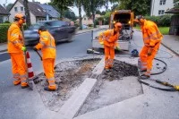 Straßenwärter brechen bei der Schadstellensanierung an einer Bushaltestelle den alten Fahrbahnbelag auf und bereiten die Erneuerung der Fahrbahn vor.