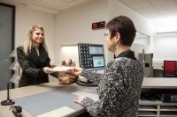 Eine Verwaltungsfachangestellte übergibt Unterlagen an eine Bürgerin.