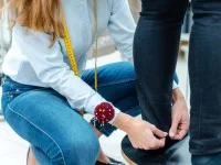 Eine Änderungsschneiderin nimmt Maß bei der Hose einer Kundin.