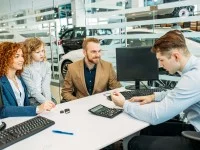 Ein Automobilkaufmann berät eine junge Familie beim Autokauf im Autohaus.