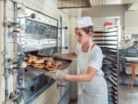 Eine Bäckerin holt frisch gebackene Brezeln und Brötchen aus dem Ofen.
