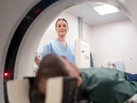 Eine medizinische Technologin für Radiologie betreut einen Patienten, der im MRT-Gerät liegt.