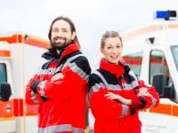 Ein Rettungssanitäterteam in roter Uniform steht vor zwei Krankenwägen, bereit für den nächsten Einsatz.