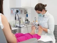 Eine Podologin behandelt die Füße einer Patientin in einer Praxis. Dabei sitzt die Patientin auf dem Behandlungsstuhl.