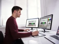 Ein Kommunikationsdesigner arbeitet mit einem Zeichenpad, zwei Bildschirmen und einem Laptop an einer neuen Werbung. 