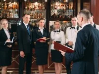 Ein Assistent für Hotelmanagement und sein Team aus sechs Mitarbeitenden stehen im Festsaal und besprechen das Menü à la carte.