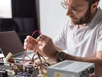 Ein Assistent für Wirtschaftsinformatik tüftelt an seinem Schreibtisch an der Hardware eines auseinandergebauten Computers.