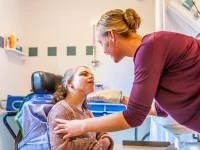 Eine Pflegeassistentin wäscht im Badezimmer ein körperlich eingeschränktes Mädchen, das im Rollstuhl sitzt, mit einem Waschlappen.