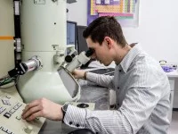 Ein physikalisch-technischer Assistent betrachtet eine Probe am Elektronenmikroskop und stellt dabei die Messwerte ein.